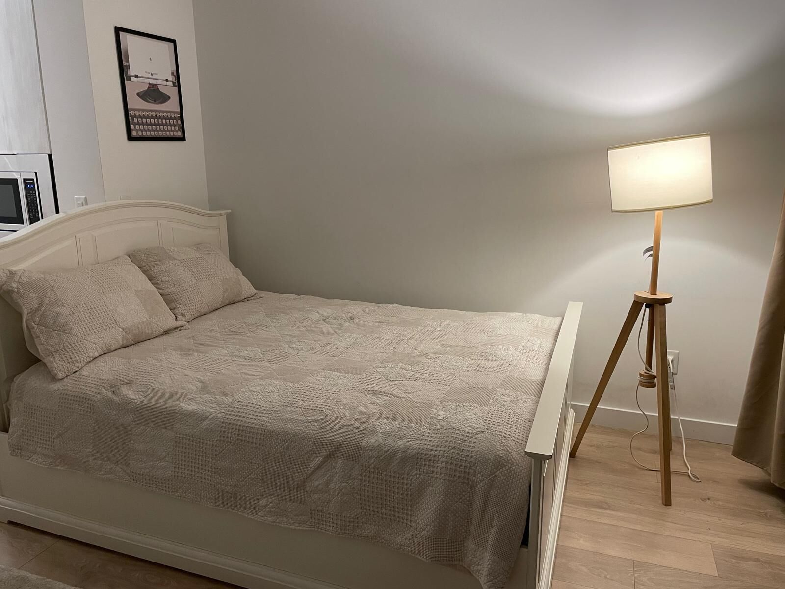 Ein ordentlich bezogenes Bett mit einer gemusterten Decke, einer Nachttischlampe und einem gerahmten Bild an der Wand.