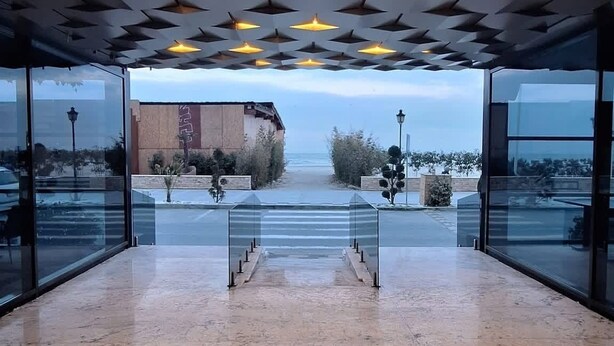 Ein Innenraum mit einem geometrischen Deckenmuster, großen Glasfenstern und Blick auf den Strand.