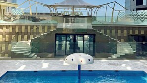 Ein Pool mit modernem Sonnenschirm, Glasgeländern und einer Treppe, die zu einem Eingang führt.