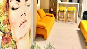 Ein modernes Wohnzimmer mit einer Couch, einem Essbereich mit gelben Stühlen und einem großen abstrakten Gemälde an der Wand.