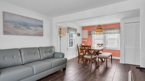 A modern living room with a gray sofa, wooden dining table, and chairs. - Professionally Managed | 3 Blocks 2 Beach (Seaside Heights)