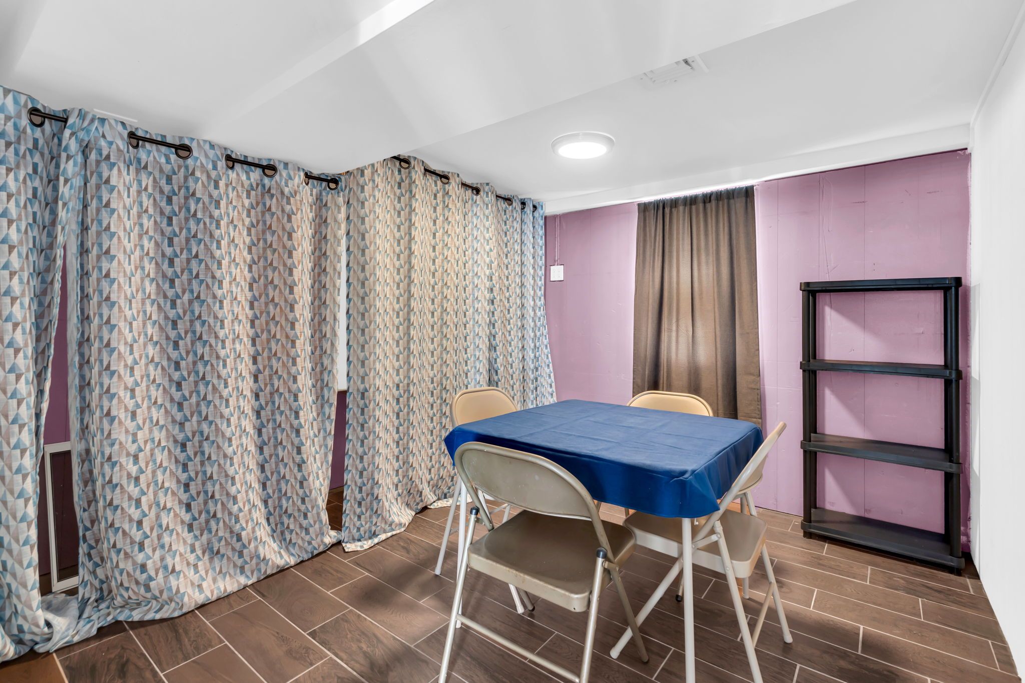 Una habitación con una mesa, sillas, una ventana con cortinas, un estante y una puerta.