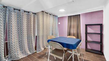 Una habitación con una mesa, sillas, una ventana con cortinas, un estante y una puerta.