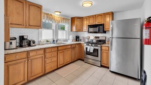 A kitchen with wooden cabinets, a stainless steel refrigerator, a microwave, a stove, and a coffee maker. - Professionally Managed | 3 Blocks 2 Beach (Seaside Heights)