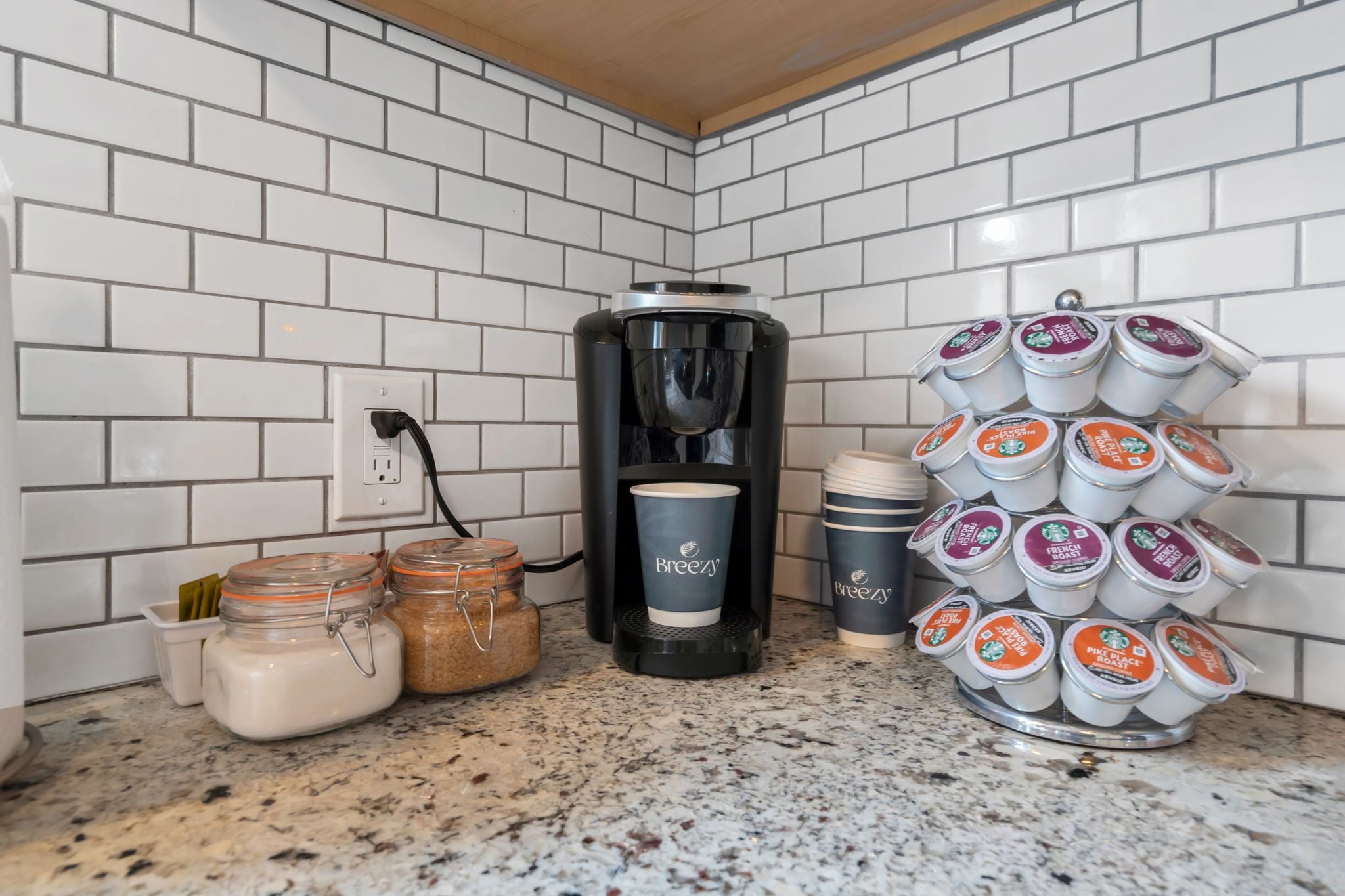 Eine Küche mit weiß gefliestem Rückspritzschutz, einer Kaffeemaschine, Gläsern und einem Becherhalter.