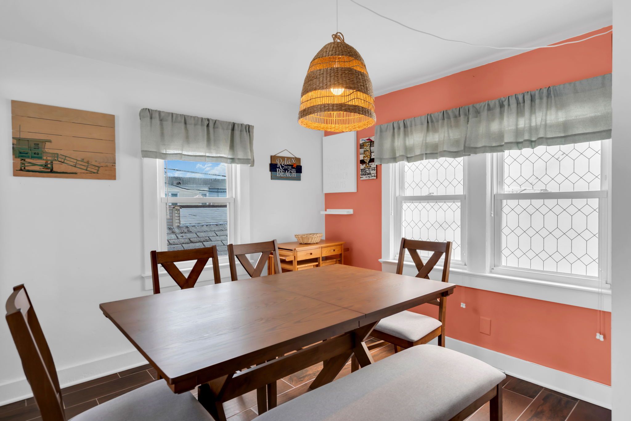 A dining area with a wooden table and chairs, a hanging light fixture, and a window with a view.