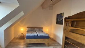 Une chambre avec un plafond en pente, un lit doté d’une tête de lit en bois, deux tables de chevet avec des lampes, un tapis et une armoire en bois.
