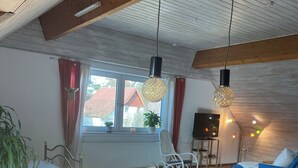 Un coin repas avec une table en bois, des chaises, une plante en pot et une vue sur un bâtiment aux toits rouges à l’extérieur.