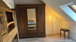 Une pièce avec un plafond en pente, une armoire en bois, une petite table et un lampadaire.