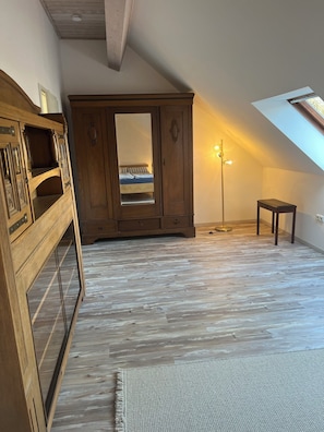 A room with a sloped ceiling, a wooden wardrobe, a small table, and a floor lamp. - Haus zur Egge - Holiday apartment in Altenbeken (Altenbeken)