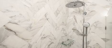 A shower with a rain showerhead and a handheld showerhead, set against a herringbone-patterned marble wall.