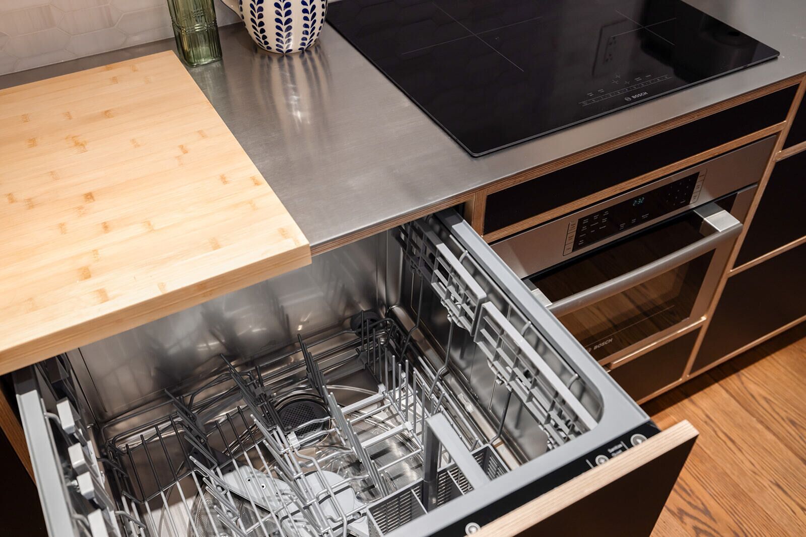 A kitchen with a dishwasher, a wooden cutting board, and a black induction cooktop.