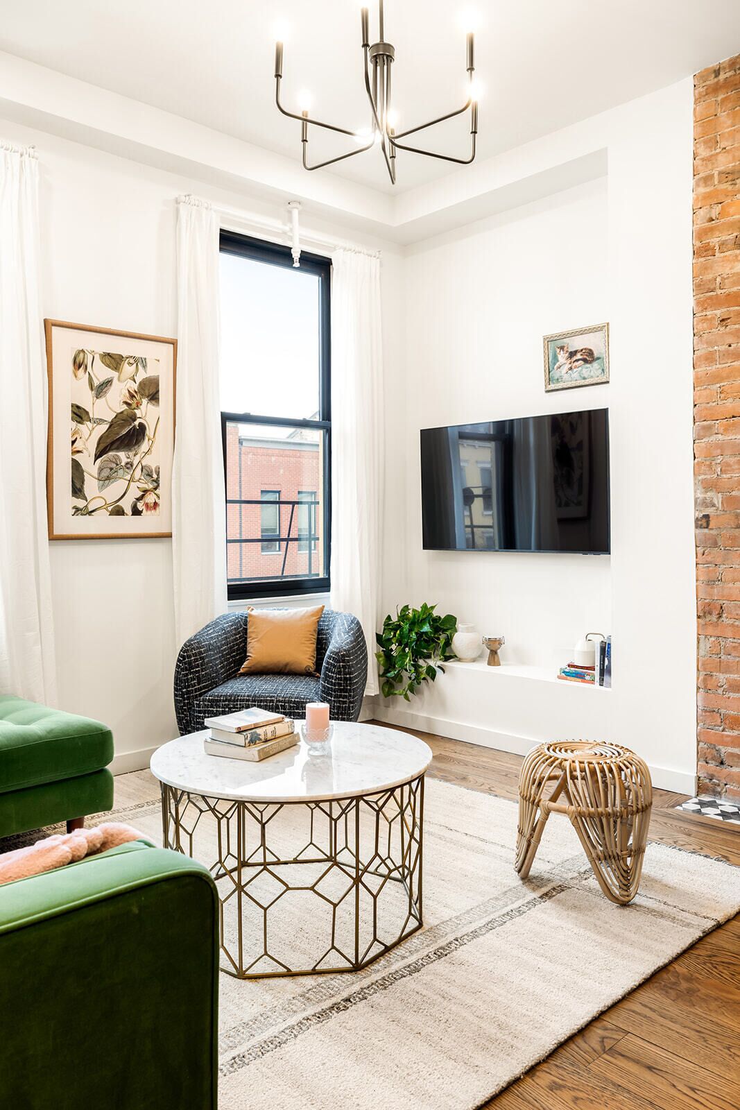 A modern living room with a green sofa, a round coffee table, a wicker ottoman, a large window, and a brick wall.