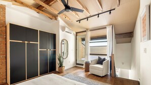 A bedroom with a bed, a wardrobe, a ceiling fan, a potted plant, and a view of the outside.