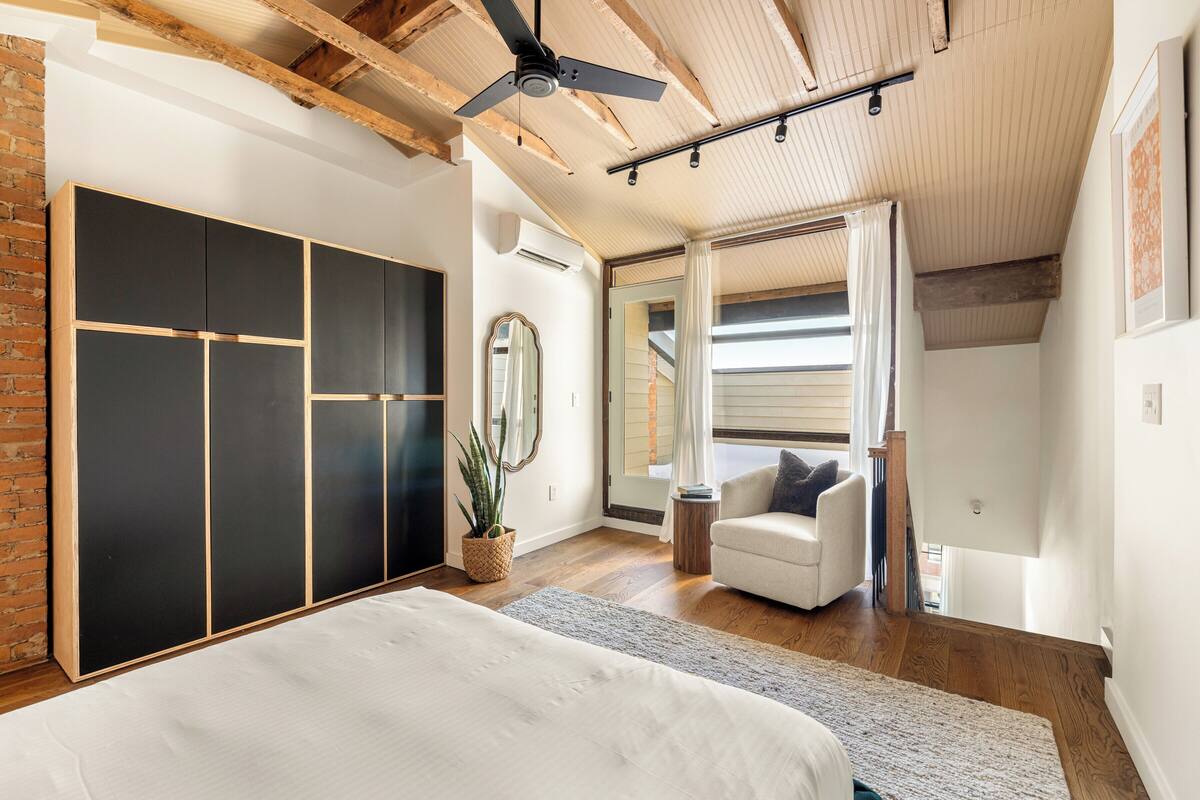 Un dormitorio con cama, armario, ventilador de techo, planta en maceta y vista al exterior.