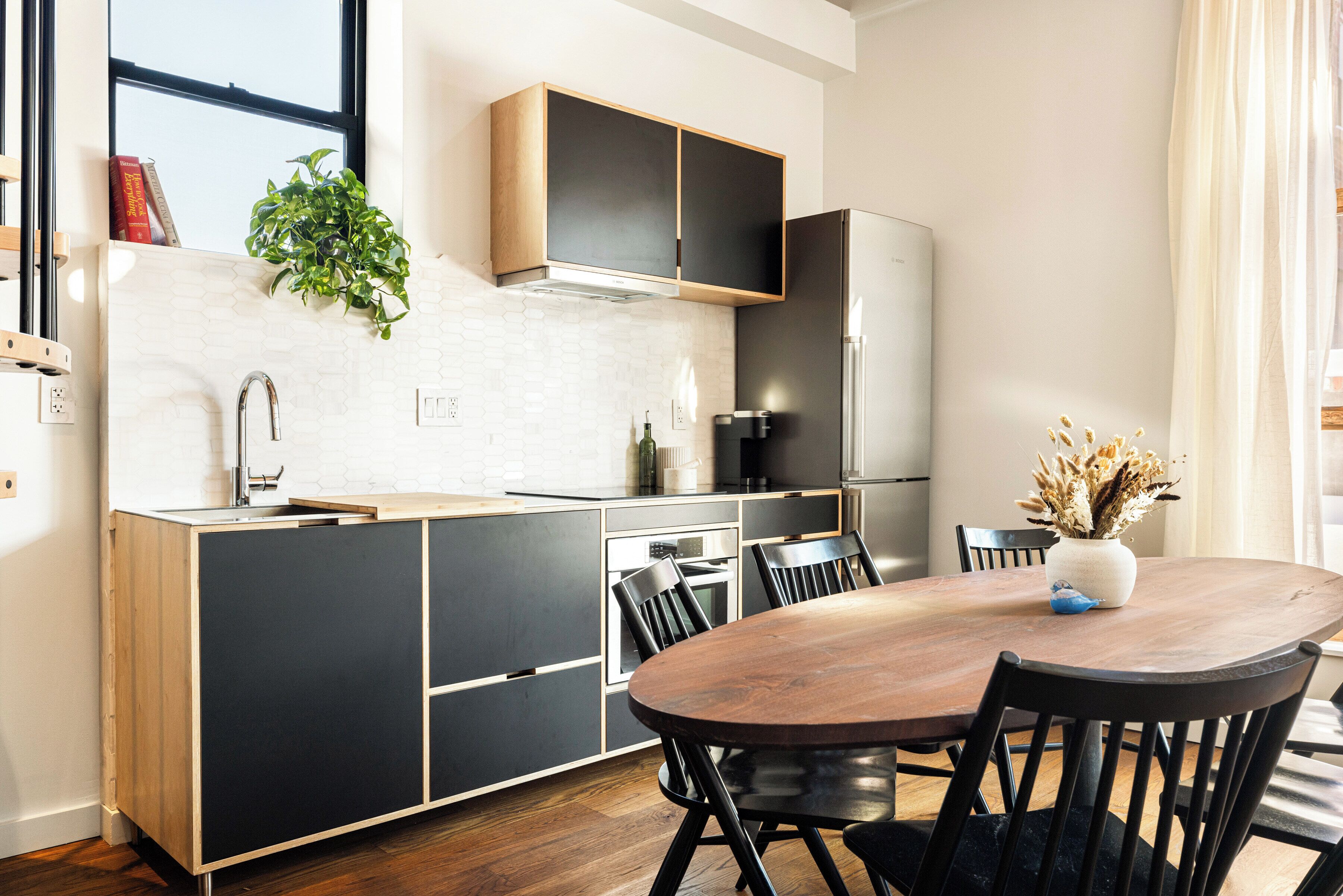 A modern kitchen with a wooden dining table, black chairs, and a built-in oven.