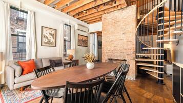 A spacious living area with a wooden dining table, comfortable seating, a brick wall, and a spiral staircase.