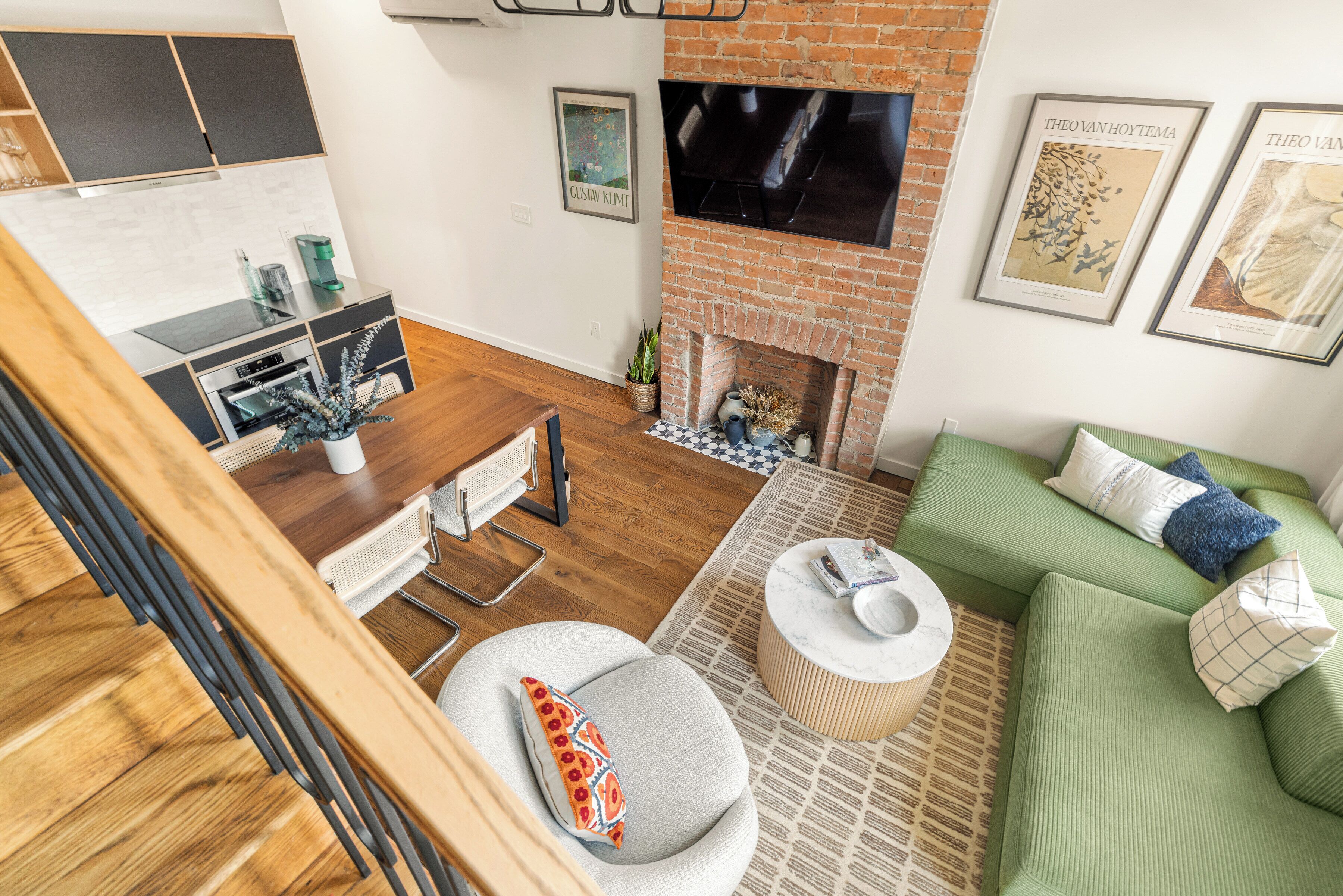 A modern living room with a fireplace, green sofa, and a dining area with a wooden table and chairs.