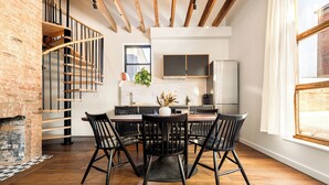 A dining area with a wooden table and chairs, a brick wall, and a spiral staircase.