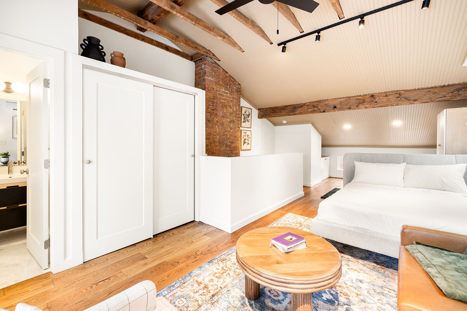 A modern interior with a white sofa, a wooden coffee table, a white wardrobe, and exposed wooden beams.
