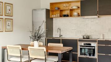 A modern kitchen with a wooden dining table, wicker chairs, a built-in oven, and a stainless steel refrigerator.