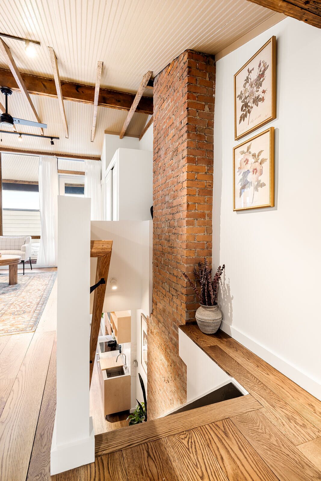 A modern interior with exposed brick, wooden beams, and a staircase leading to an upper level.