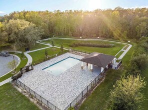 Ein Schwimmbecken mit einer Steindeck, umgeben von einem Zaun, und einem überdachten Pavillon.