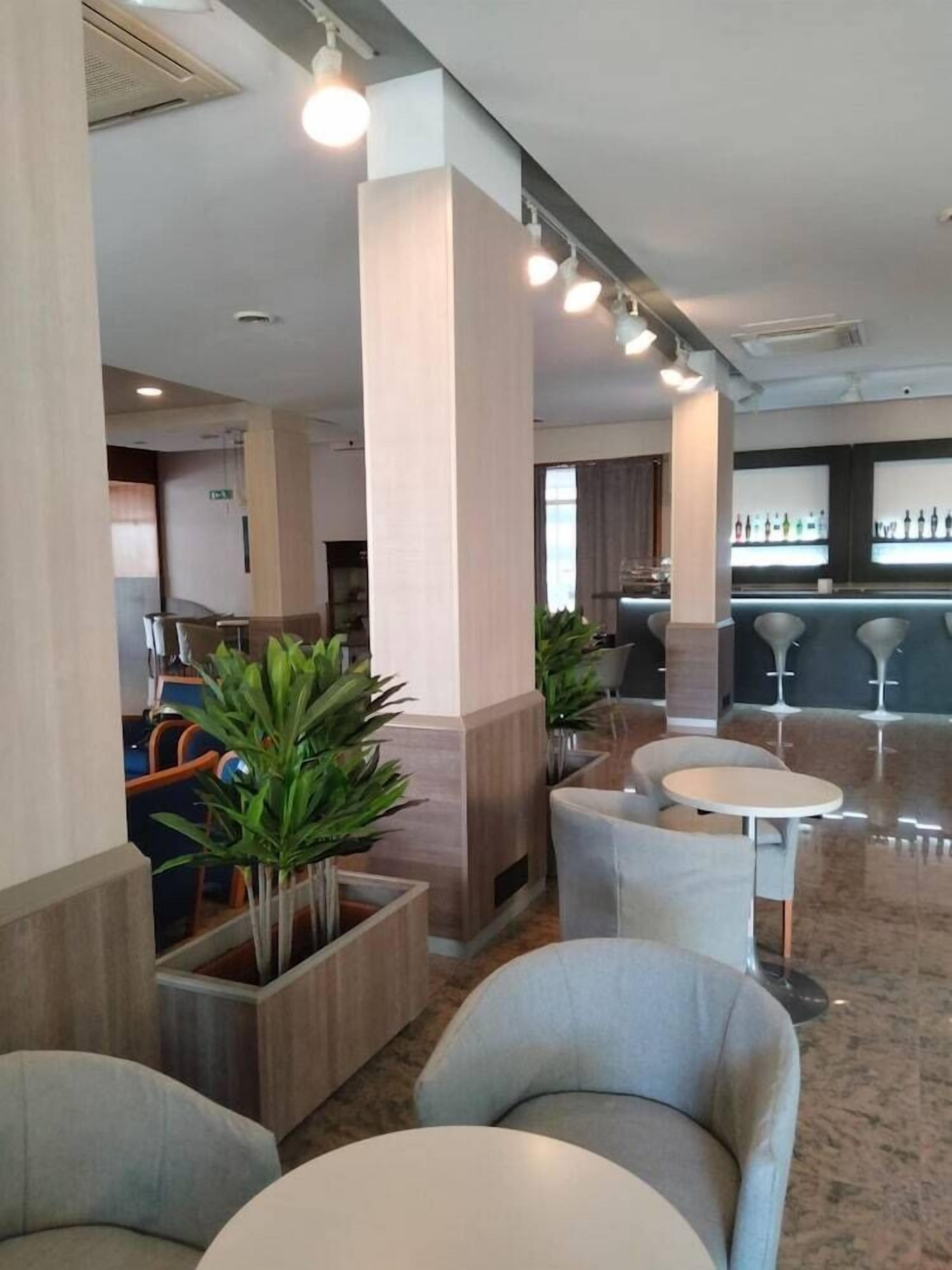 A modern hotel lobby with seating areas, a bar, and potted plants.