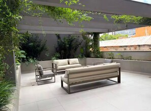 An outdoor seating area with a sofa and chairs, surrounded by greenery and a pergola. - Queen bed with Emma mattress, air conditioning, double shower, and Nespresso coffee machine. (São Paulo)