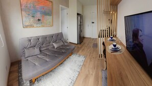 Uma sala de estar moderna com um sofá cinza, um quadro, uma mesa de jantar de madeira com pratos azuis e brancos, e uma televisão.