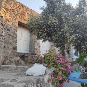 A stone building with a white door, a table, and a large rock. - Charming Holiday House in Mikonos With Garden View (Mykonos)