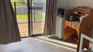 Una habitación con puerta de vidrio corredera que da a un balcón, una kitchenette equipada con microondas, tostadora y cafetera, y un escritorio de madera con silla.