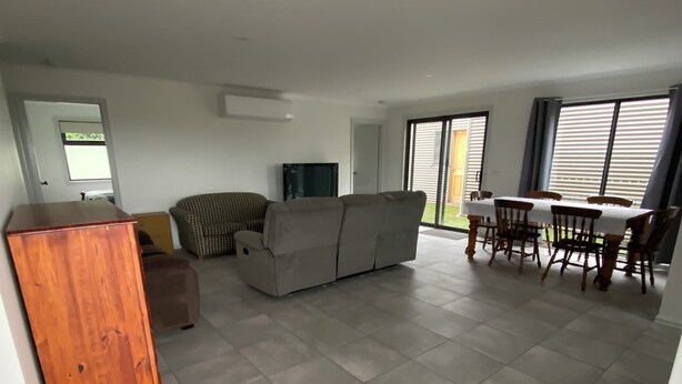 Un espacio habitable amplio con un sofá, un mueble de madera, un televisor y una mesa de comedor con sillas.