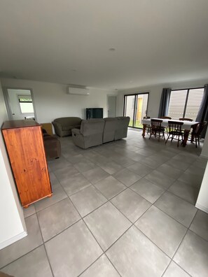A spacious living area with a sofa, a wooden cabinet, a television, and a dining table with chairs.