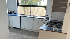 Una cocina con armarios blancos, estufa a gas, microondas y ventana con vistas a árboles.