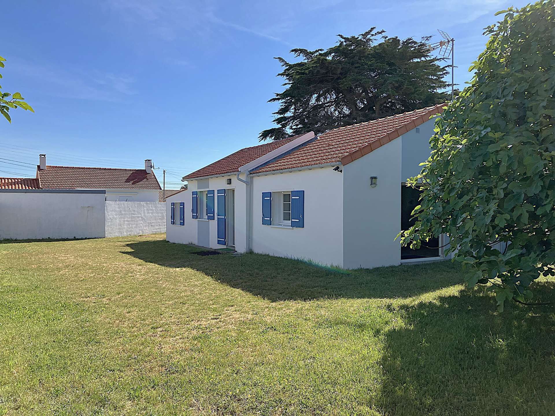 Une maison de plain-pied avec un toit en tuiles, un petit jardin devant et un arbre en arrière-plan.