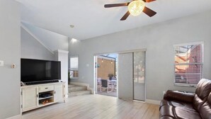 Un soggiorno con TV, ventilatore a soffitto e una porta scorrevole in vetro che dà su un patio esterno.