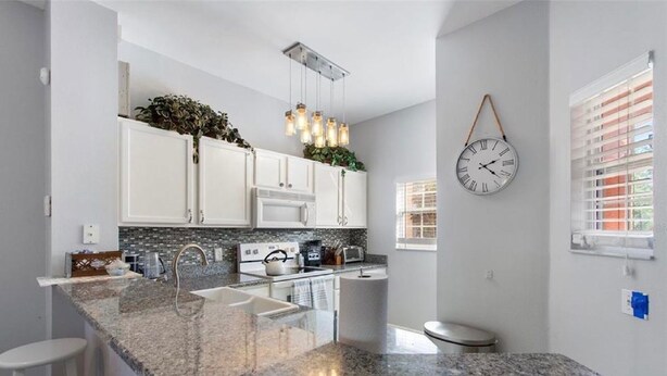 Una cucina moderna con piani in granito, pensili bianchi, forno integrato e lampadario.
