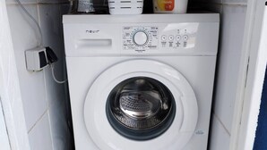 A compact, white front-loading washing machine in a small laundry room with tiled walls and a blue trim. - Charming Ground Floor Apartment With Sea Views in Bueu (Bueu)