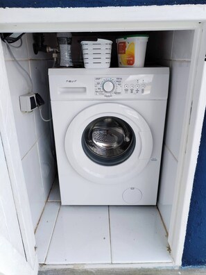 Eine kompakte, weiße Waschmaschine mit Frontlader in einem kleinen Waschraum mit gefliesten Wänden und blauer Bordüre.