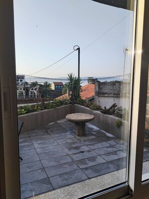 Ein Balkon mit einem Steintisch, einem Blumentopf und Blick auf Gebäude sowie einen Berg im Hintergrund.