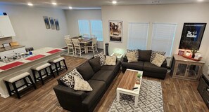 Ein modernes Wohnzimmer mit einem schwarzen Sofa, einem Couchtisch und einem Essbereich mit rot-weißer Tischdecke.