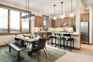 A modern kitchen with wooden cabinets, a stainless steel refrigerator, and a dining area with a bench and chairs. - Downtown WP Condo F-202 I Private Hot Tub I Great Views I Bunk Room I Discounted Attractions (Fraser)