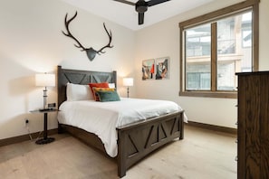 A bedroom with a bed, a ceiling fan, a window, and artwork on the wall. - Downtown WP Condo F-202 I Private Hot Tub I Great Views I Bunk Room I Discounted Attractions (Fraser)
