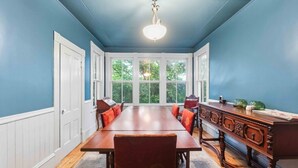 A dining room with a long table, red chairs, a wooden cabinet, and a view through large windows. - Gaspereau Heritage House - Annapolis Valley (Wolfville)