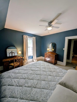 A bedroom with a bed, a desk, a dresser, a ceiling fan, and a window with curtains.