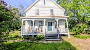 A white two-story house with a porch, number 29, surrounded by greenery. - Gaspereau Heritage House - Annapolis Valley (Wolfville)