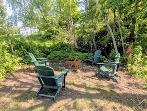 Une zone boisée avec quatre fauteuils Adirondack verts et une petite boßte en bois.