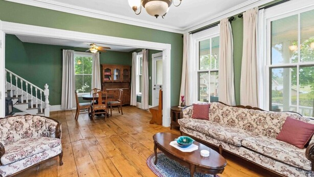 A spacious living room with a wooden floor, a sofa, two armchairs, a dining table, and a chandelier. - Gaspereau Heritage House - Annapolis Valley (Wolfville)