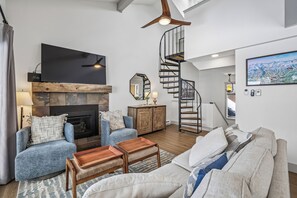 A modern living room with a fireplace, blue armchairs, a wooden coffee table, a spiral staircase, and a large painting. - 4 O'Clock Lodge D27: Remodeled condo close to town and the slopes - New Listing. (Breckenridge)